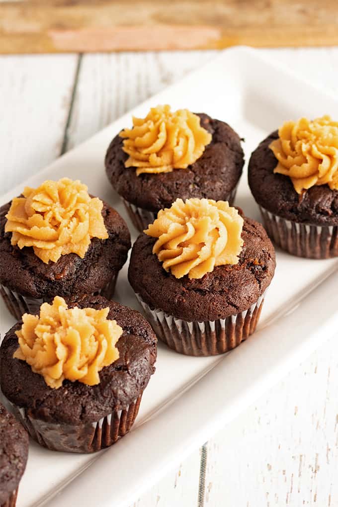 Top down view of chocolate zucchini cupcakes on a white platter with a white wooden background