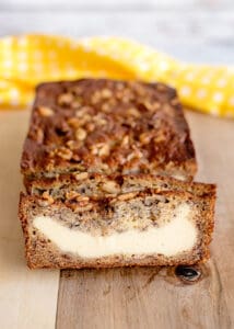 sliced cream cheese banana bread on a cutting board with a yellow polka-dotted fabric behind it