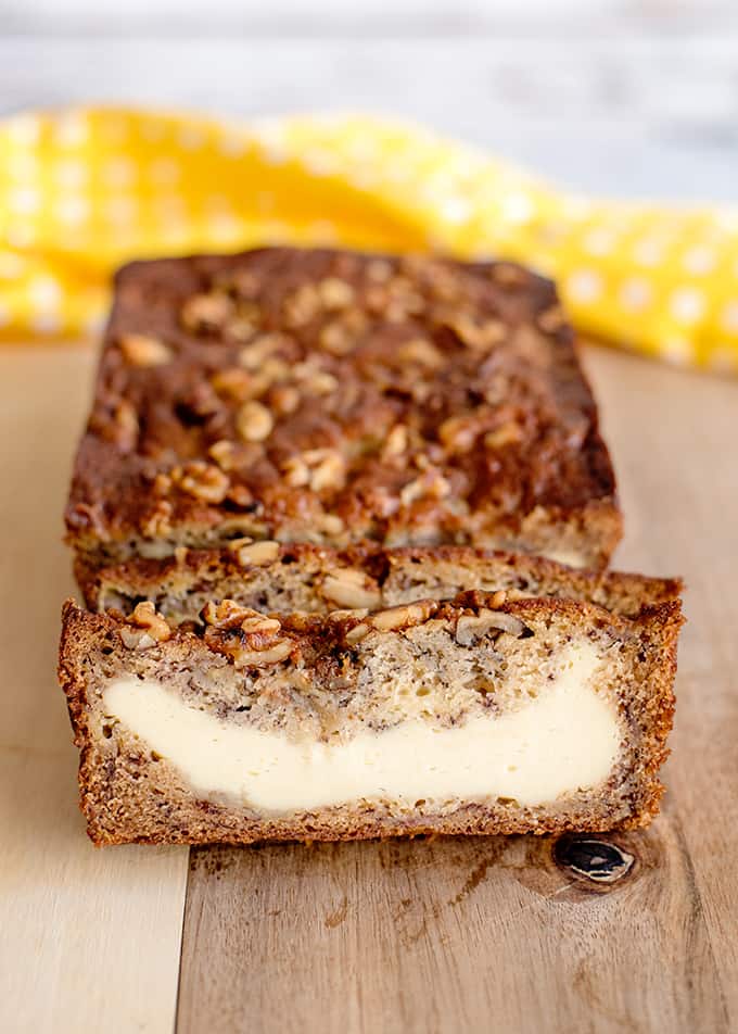 sliced cream cheese banana bread on a cutting board with a yellow polka-dotted fabric behind it