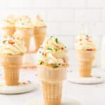 Ice cream cones topped with sprinkles served on a white plate.
