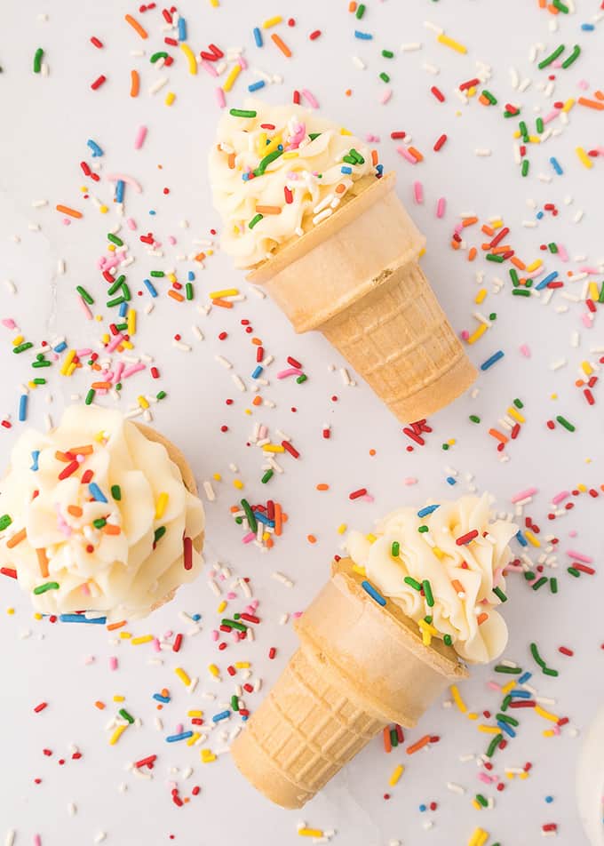 ice cream cone cupcakes laying down on a counter with sprinkles.