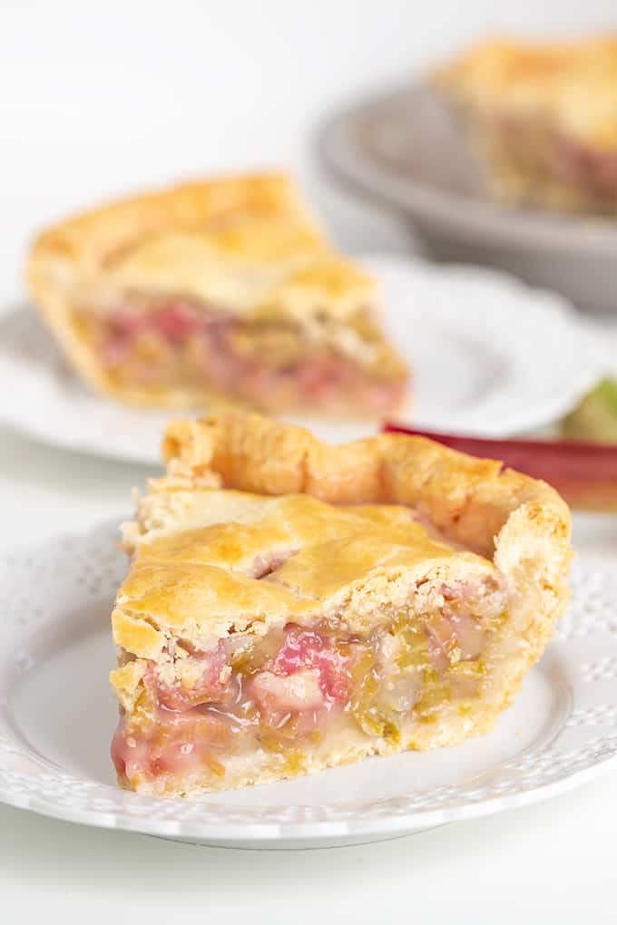 Slice of rhubarb pie on a white plate with a second slice nehind it, close up, side view, showing filling.