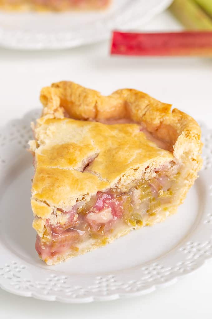 Single slice of rhubarb pie in focus on a white lace plate on a white background