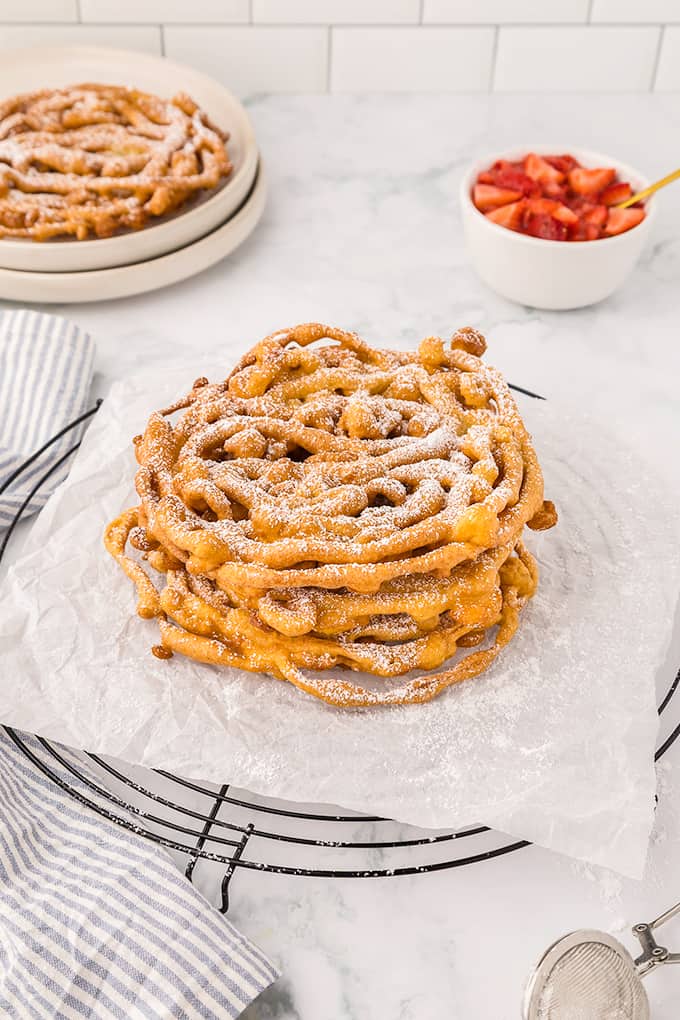 A plate of Homemade Funnel Cakes with powdered sugar and strawberries.