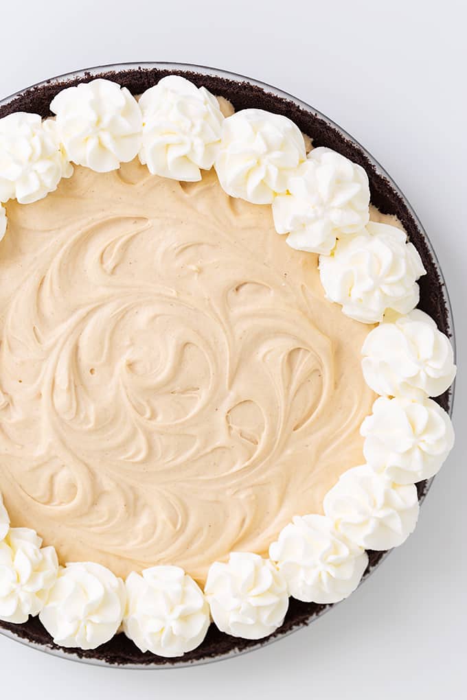 overhead photo of a peanut butter pie with an oreo crust and whipped cream on top on a white background
