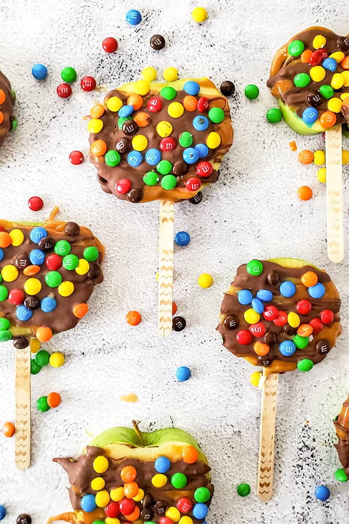 Caramel apple slices with chocolate and M&M's on a stick. on a marble surface