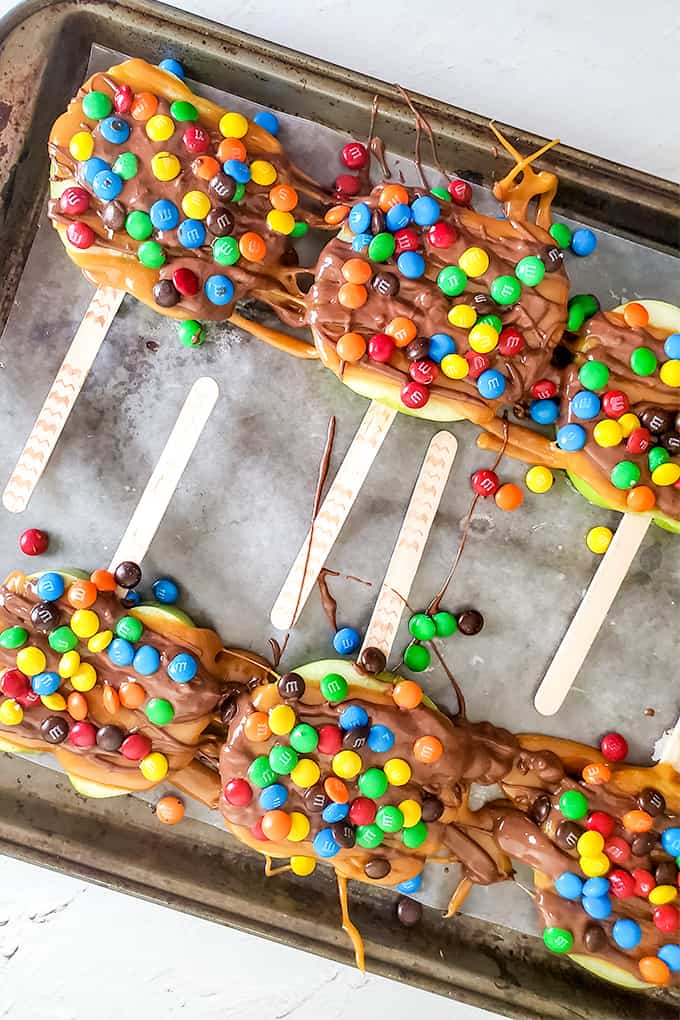 Caramel apple slices with popsicle sticks arranged on a baking sheet with parchment paper