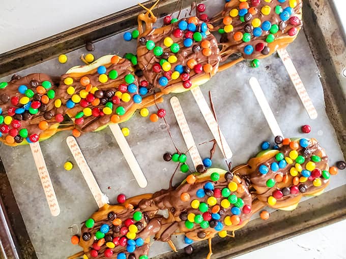 Chocolate covered caramel apple slices on a baking sheet.