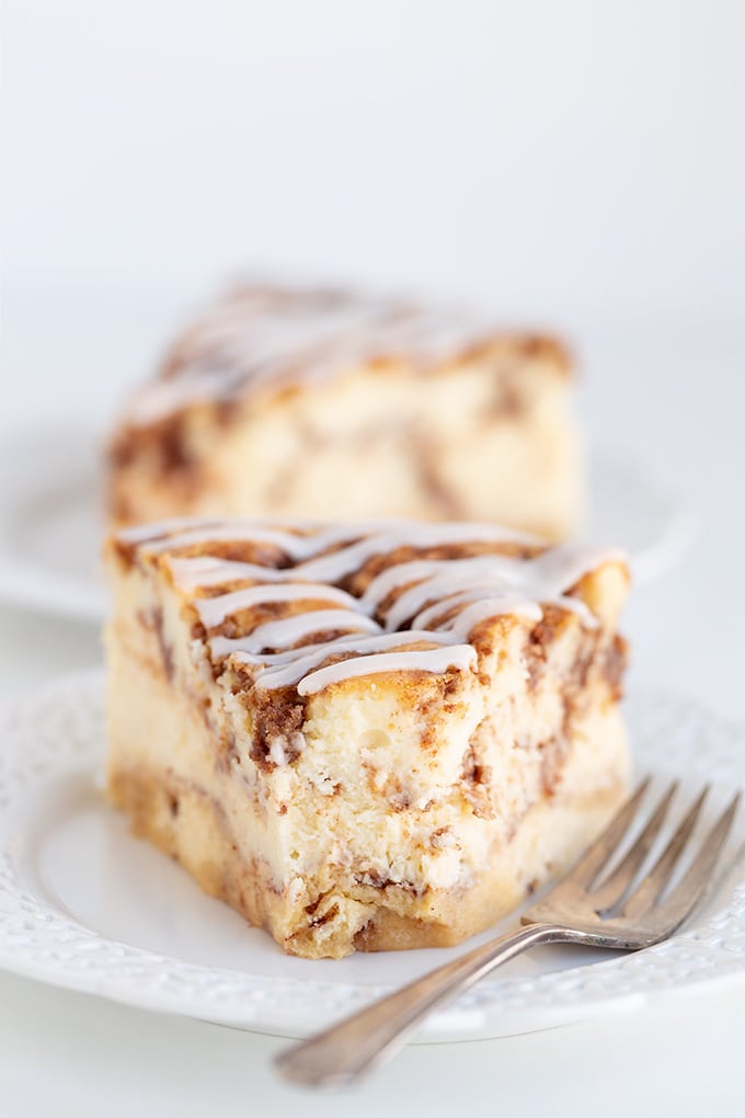 A slice of cinnamon roll cake drizzled with cream cheese icing, presented on a plate with a fork.