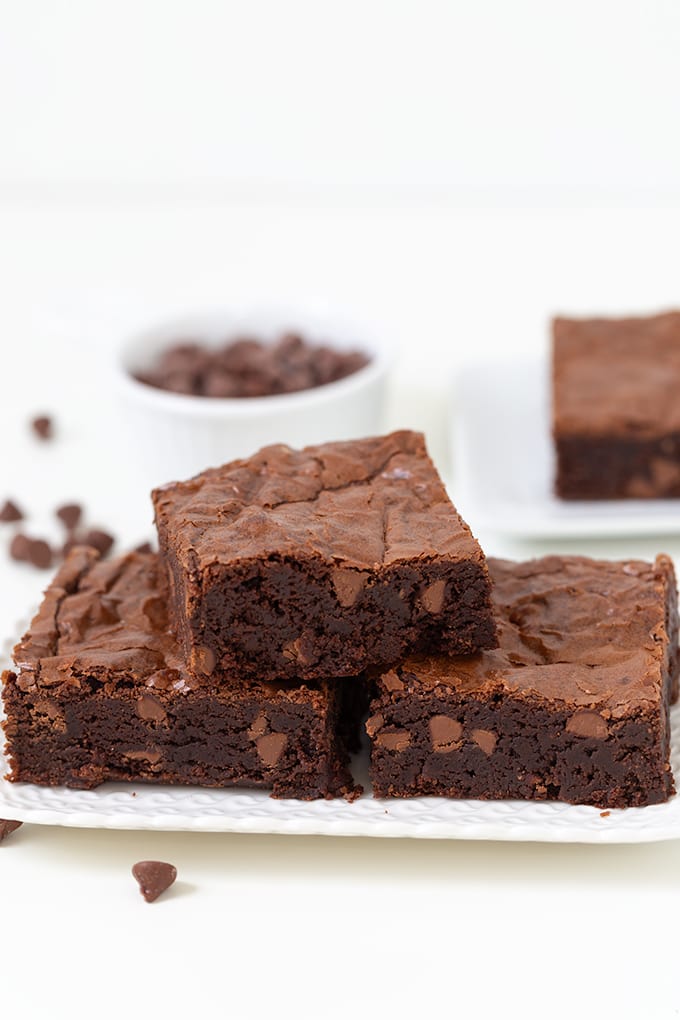 A stack of rich chocolate brownies enhanced with a touch of creativity, served on a pristine white plate with a small white bowl of chocolate chips