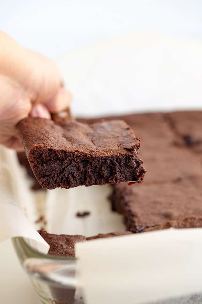 A person is holding a homemade brownie out of a pan.