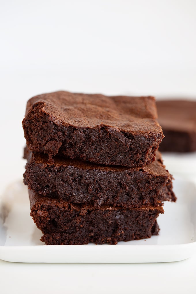 Homemade chocolate brownies stacked on a white square plate on a white surface