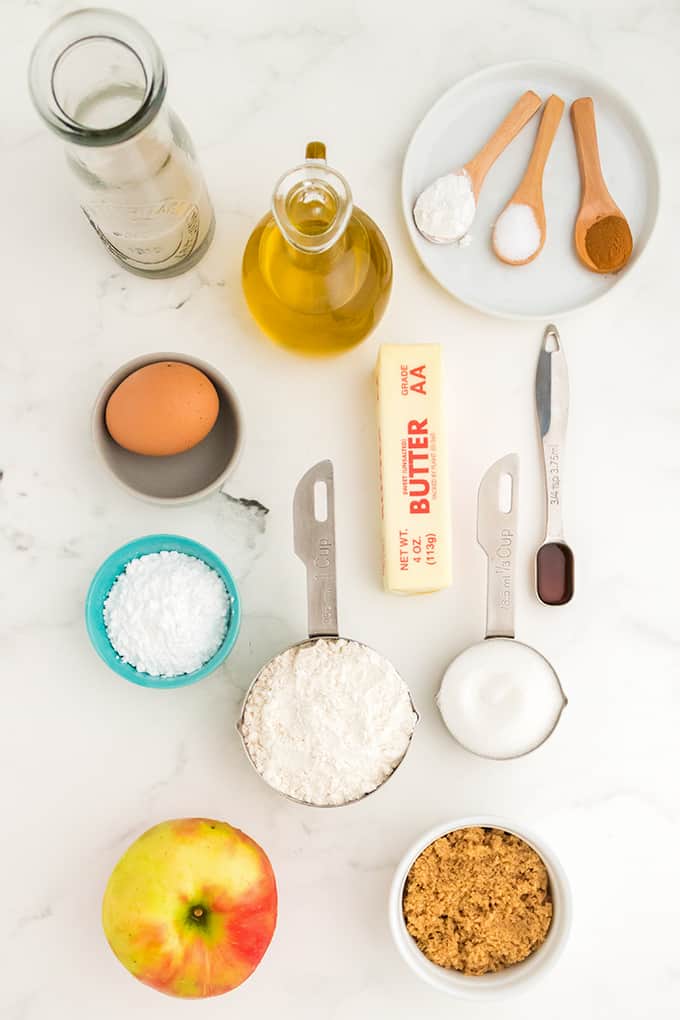 The ingredients for apple pie, including apples and cinnamon, are laid out on a table.