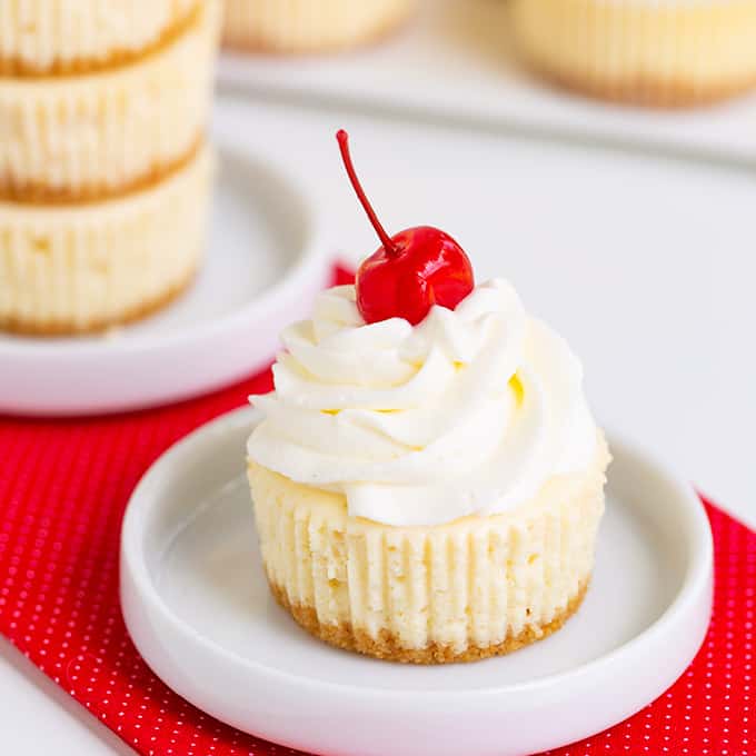A plate of mini cheesecakes with a cherry on top.