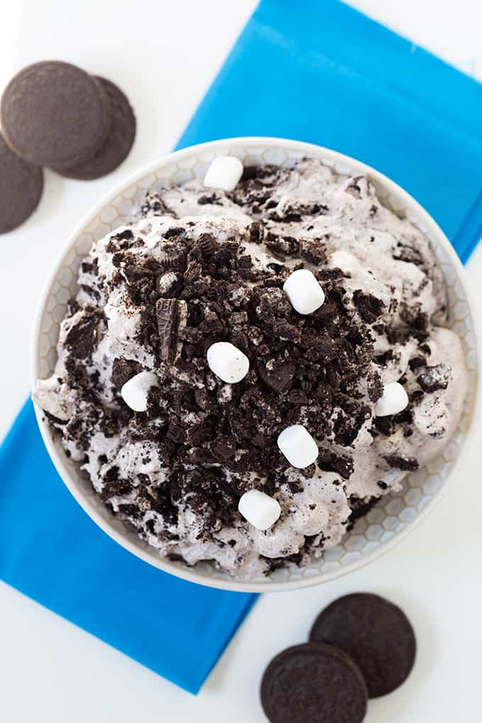 Oreo cheesecake salad in a white bowl with a bright blue linen under it on a white surface with chocolate cookies