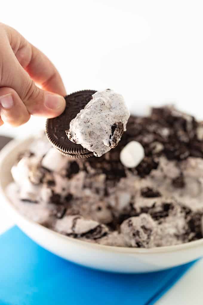 A person holding a scoop of Oreo Fluff on an Oreo with the serving bowl. behind it