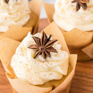 Three apple cider cupcakes with icing and star anise on a wooden board.