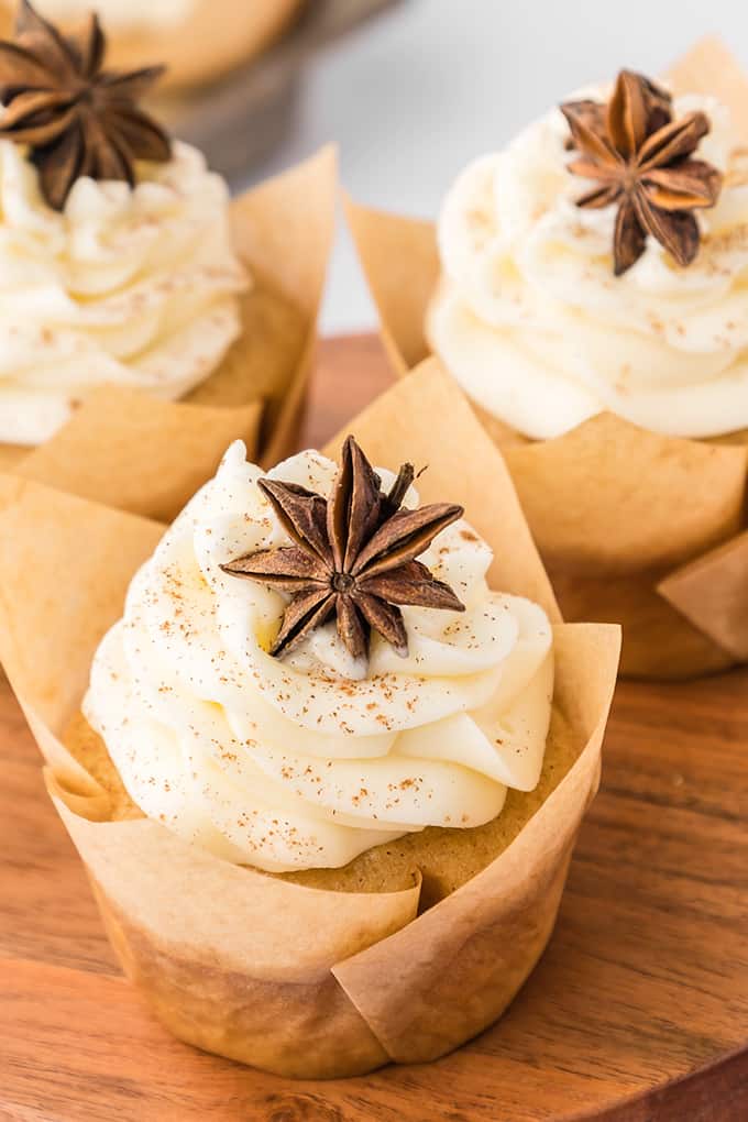 Three apple cider cupcakes with icing and star anise on a wooden board.