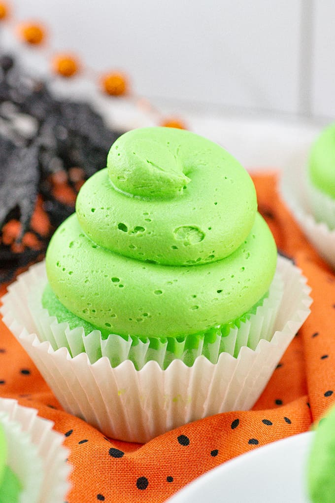 halloween slime cupcakes with green frosting on it. on an orange linen