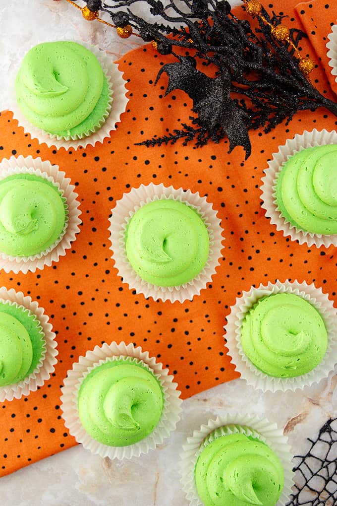 A group of lime cupcakes on an orange and black linen on a table