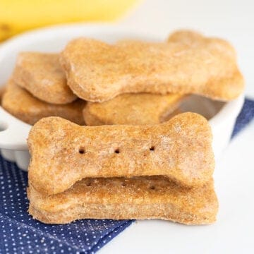 A bowl of dog treats next to a banana.