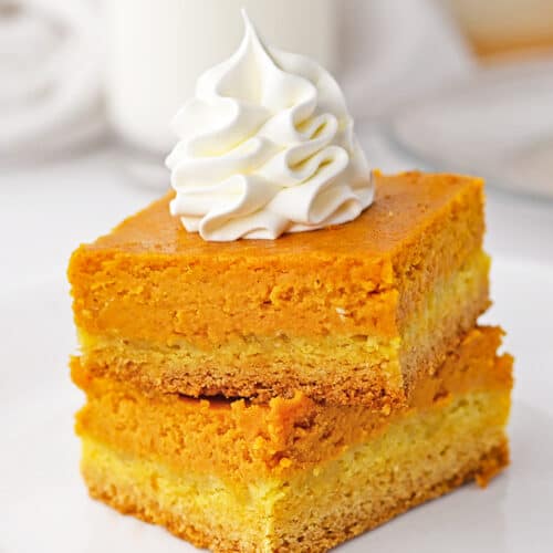 A stack of Pumpkin Gooey Bars on a white plate with whipped cream piped on top