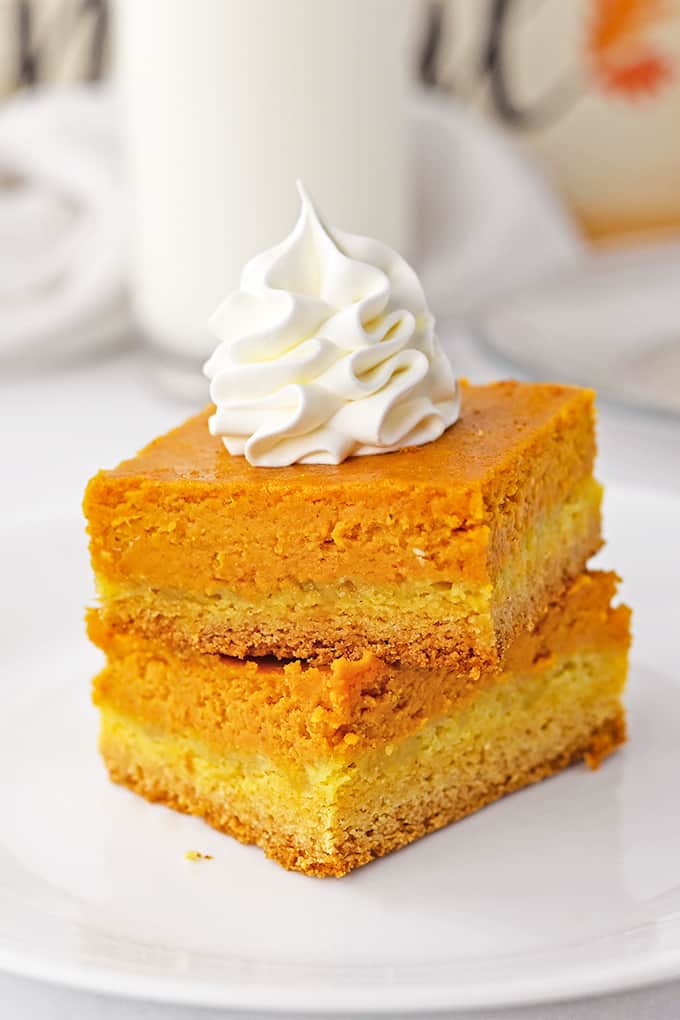 A stack of Pumpkin Gooey Bars on a white plate with whipped cream piped on top