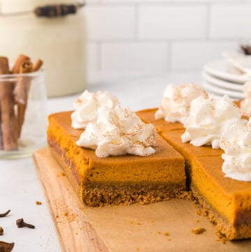 Pumpkin pie bars with whipped cream on a cutting board with brown parchment paper