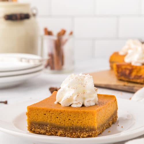 Pumpkin pie bars with whipped cream on top on a white plate on a white surface