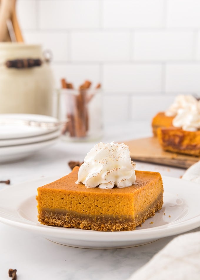 Pumpkin pie bars with whipped cream on top on a white plate on a white surface