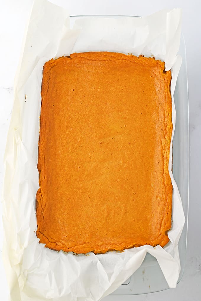 baked pumpkin gooey bars in a baking dish with parchment paper on a marble counter