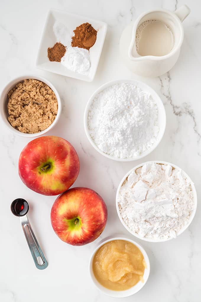 Apple fritters and pie ingredients on a white marble table.