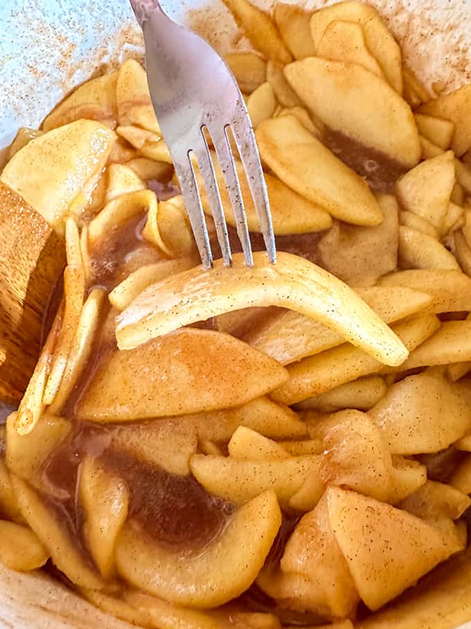 The Best Apple Pie is being prepared using a fork to stir apples in a bowl.