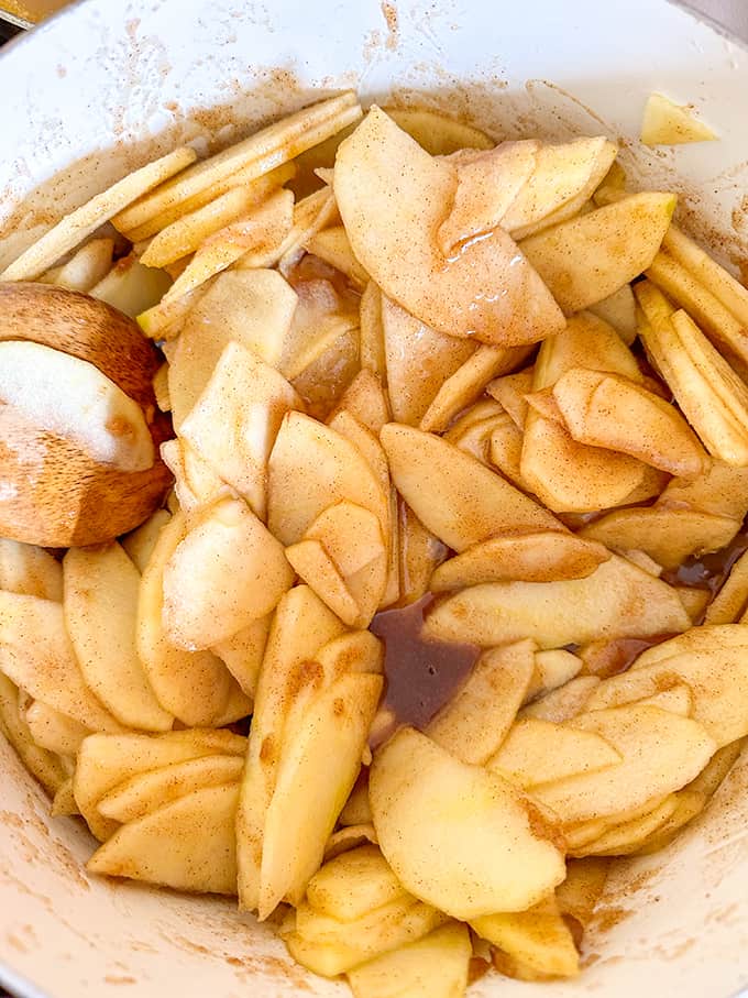 Apple slices in a bowl with a wooden spoon for The Best Apple Pie.