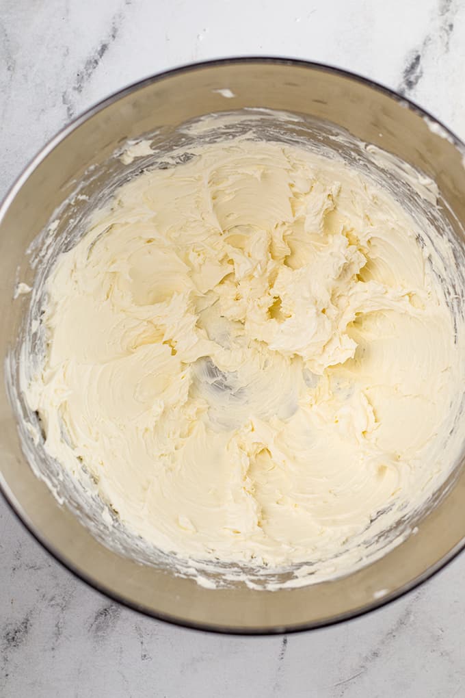 cream cheese in a metal mixing bowl on a marble countertop.