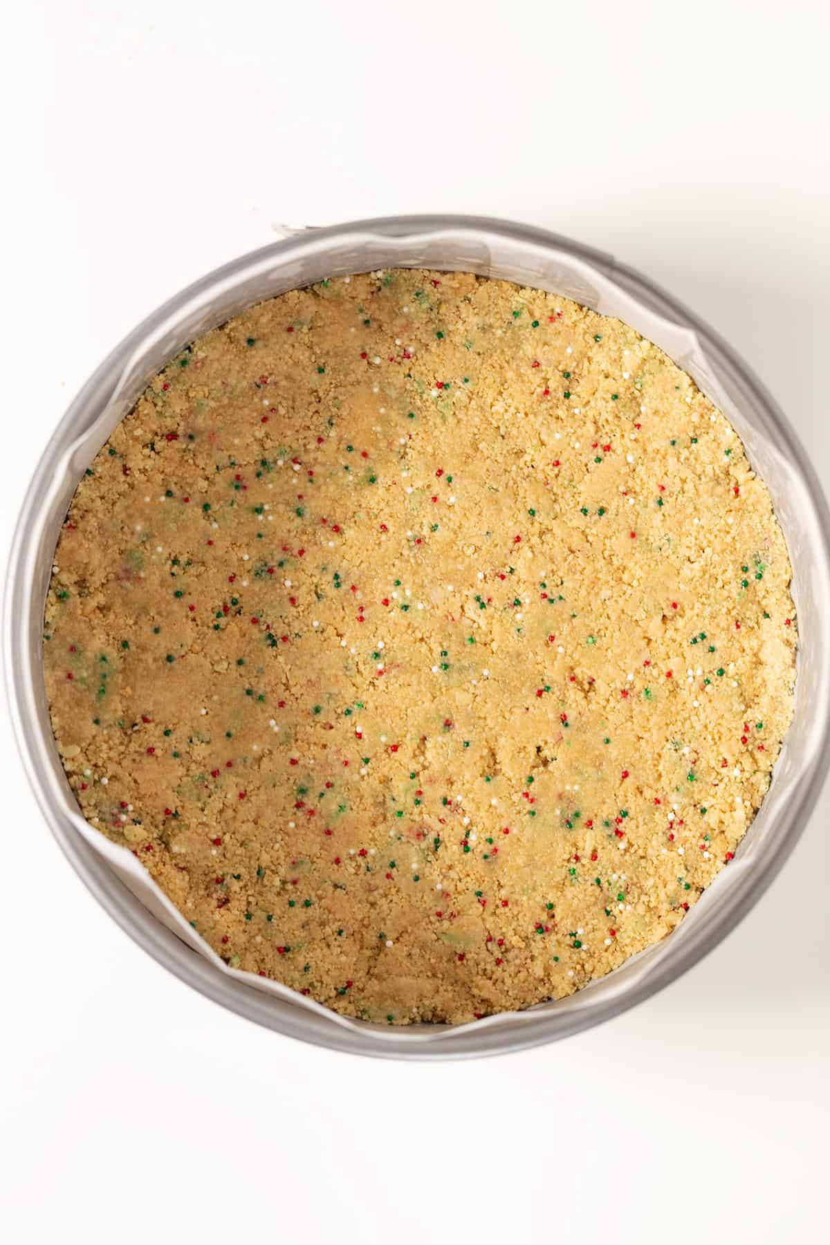 A Christmas Tree Cheesecake with sprinkles in a pan on a white surface.