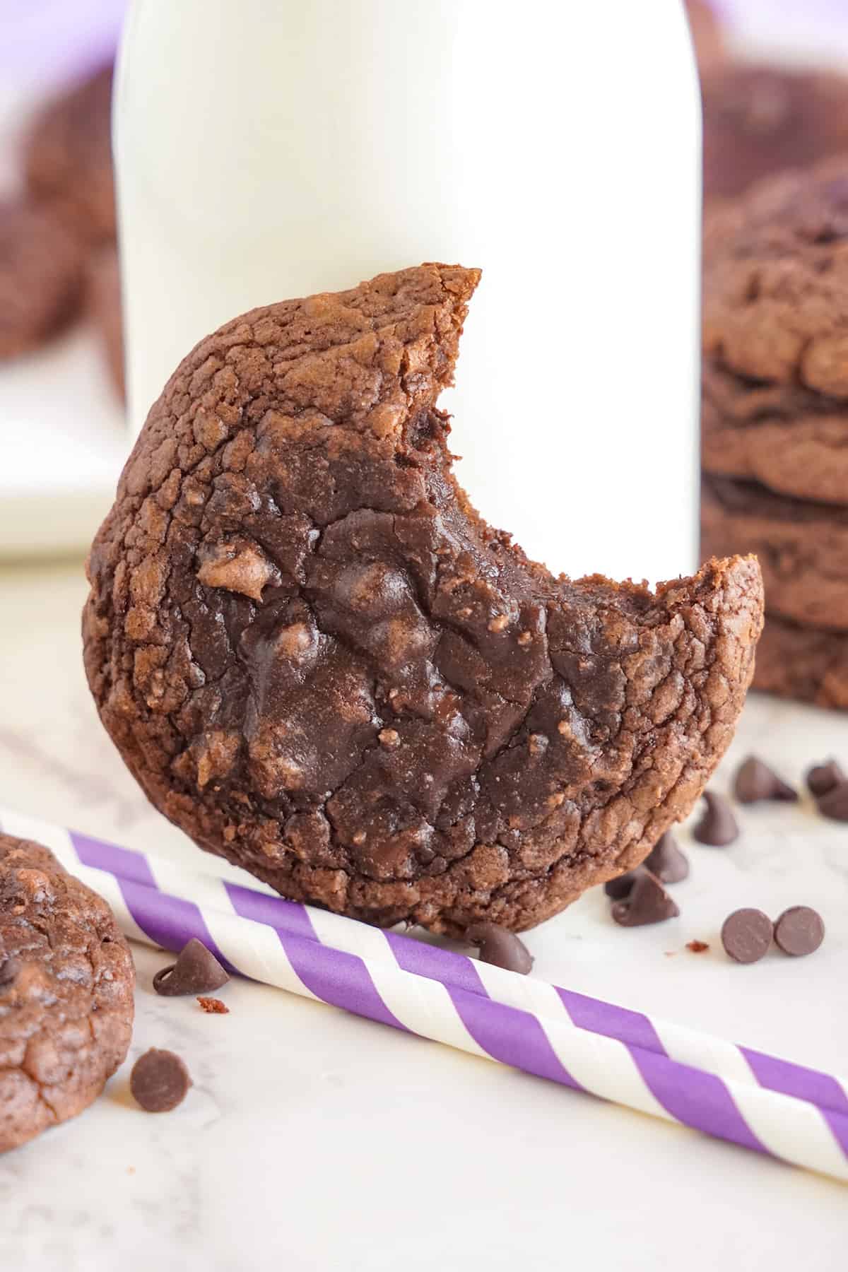 A chocolate cookie with a bite taken out of it next to a glass of milk.