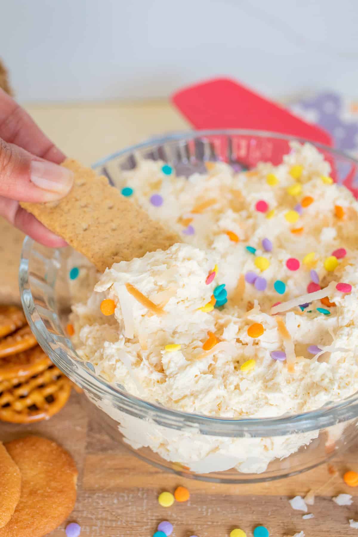 A person dipping a biscuit into a bowl of colorful sprinkle-topped coconut cream dip.