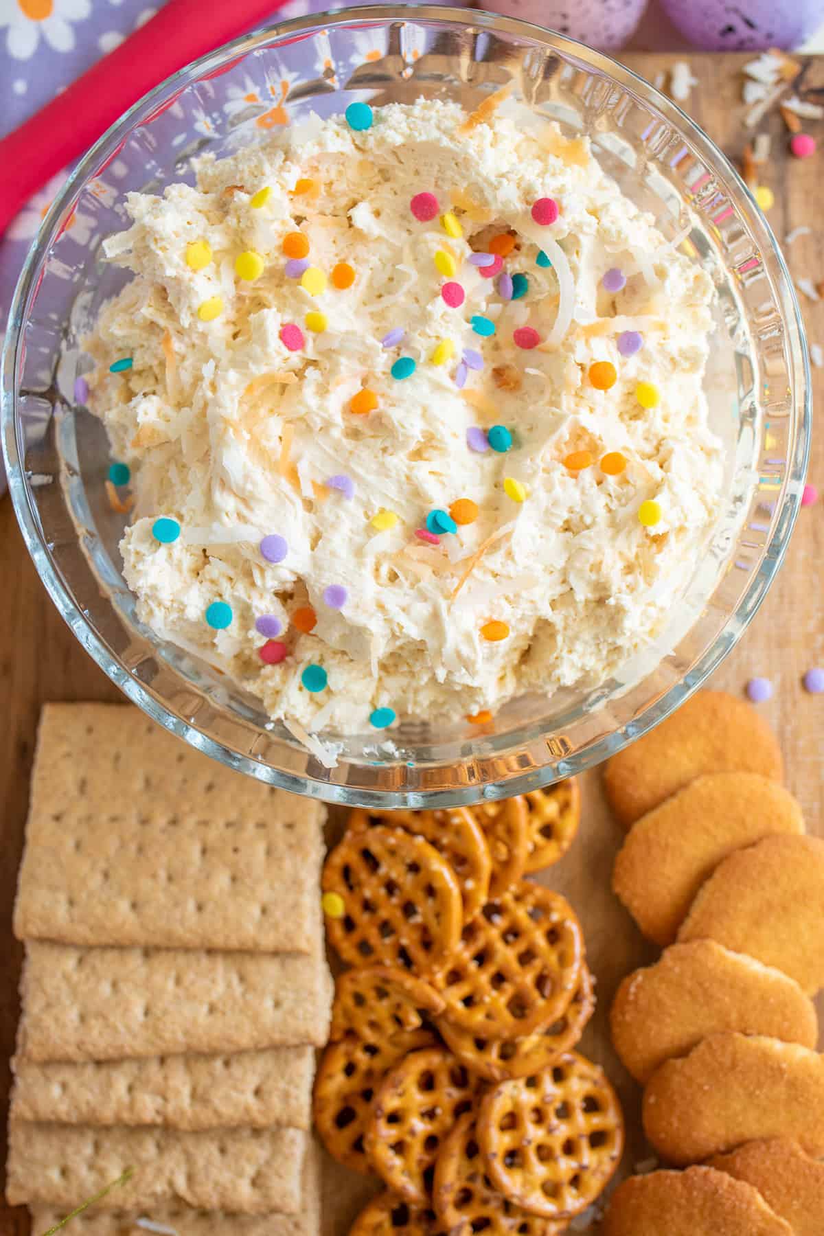 A bowl of coconut cream dip sprinkled with colorful toppings, surrounded by an assortment of crackers and cookies.