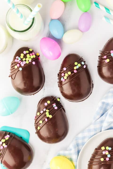Decoratively iced chocolate Easter eggs, including copycat Creme Eggs, accompanied by pastel-colored plastic eggs and festive straws.