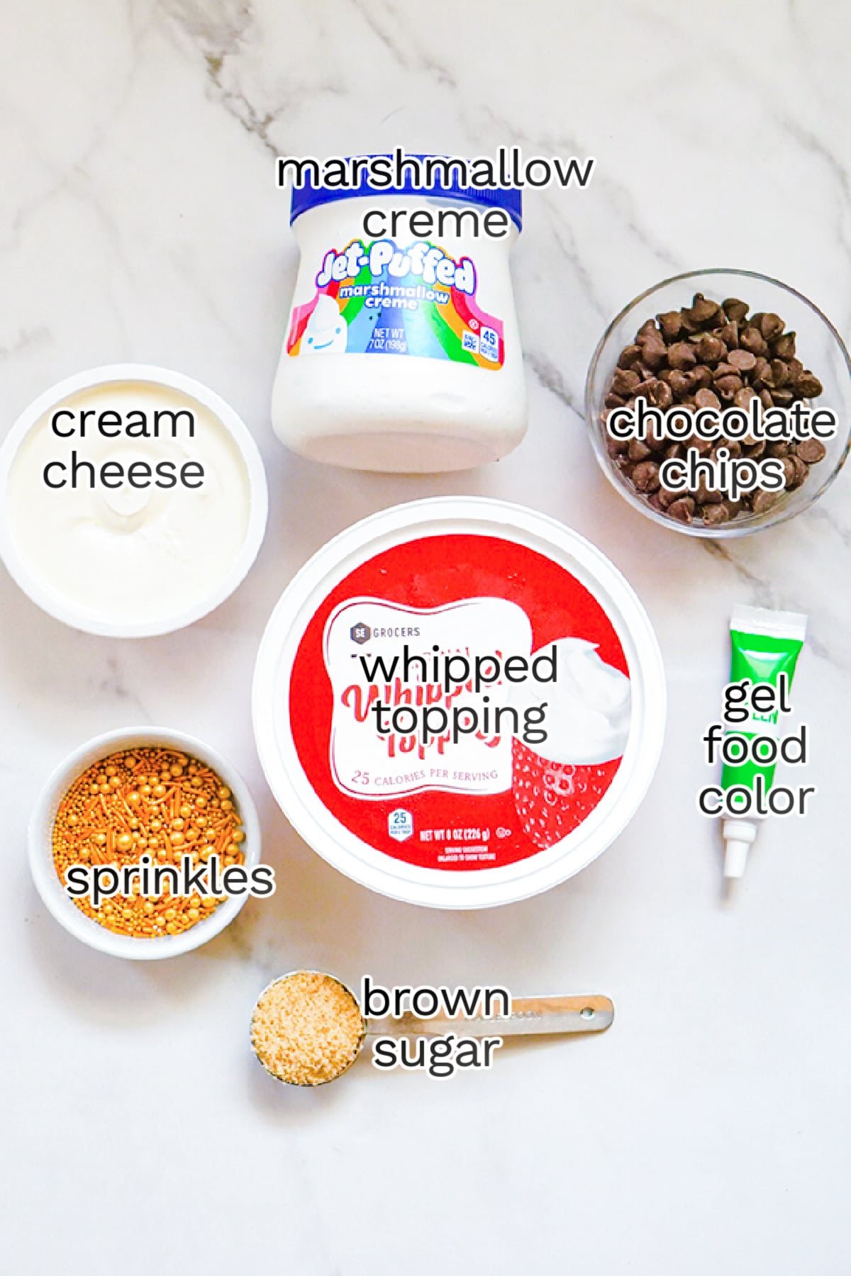 Ingredients for a St. Patrick's Day Booty Dip recipe displayed on a marble countertop, labeled: cream cheese, marshmallow creme, whipped topping, brown sugar, sprinkles, chocolate chips