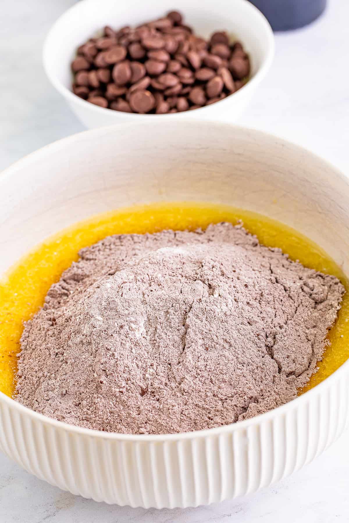 Ingredients for baking Baileys cupcakes in separate bowls: melted butter and dry cocoa mix in the foreground, chocolate chips in the background.