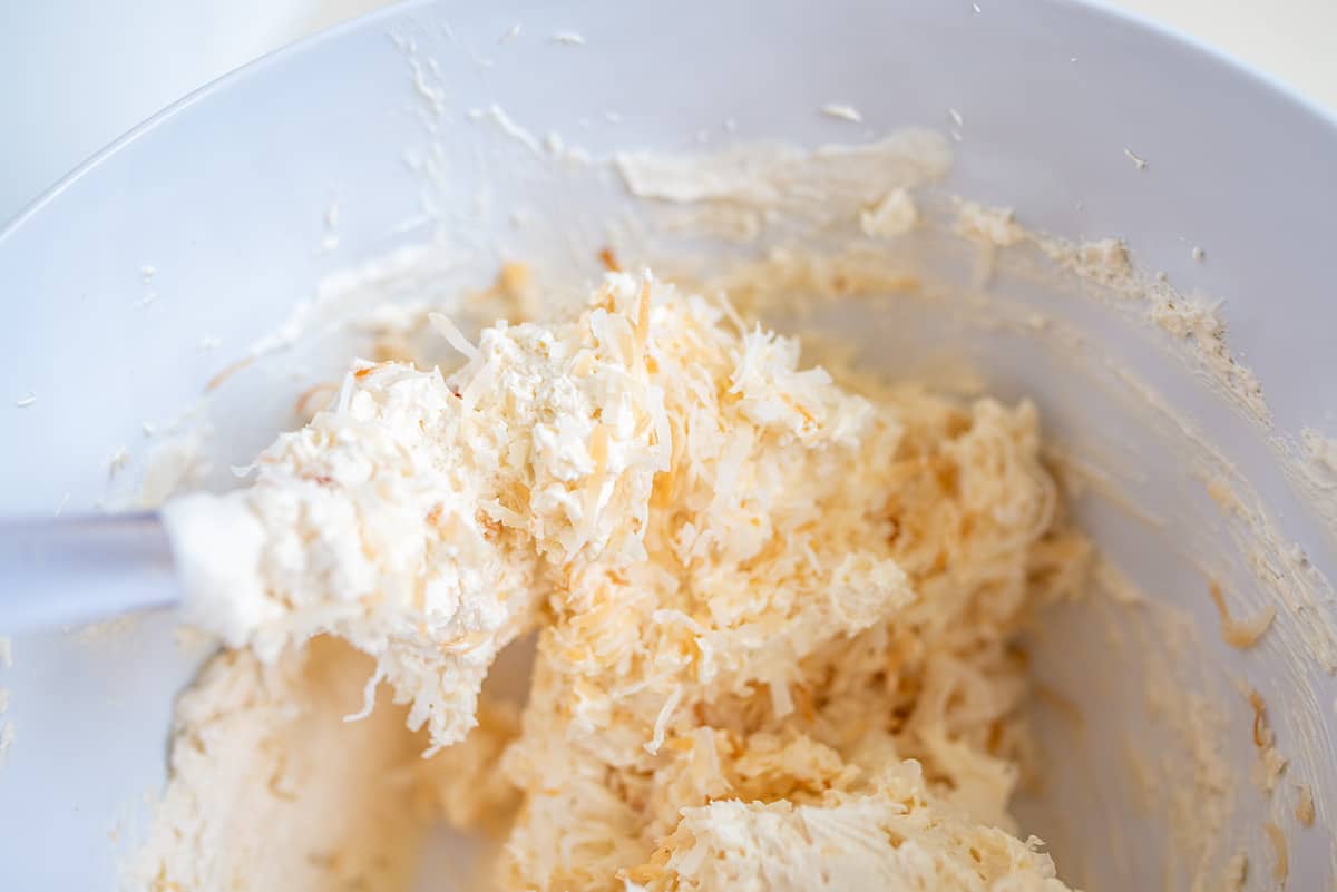 A bowl containing a mixture of ingredients for a Coconut Cream Dip with a spatula, likely in the process of baking or cooking.