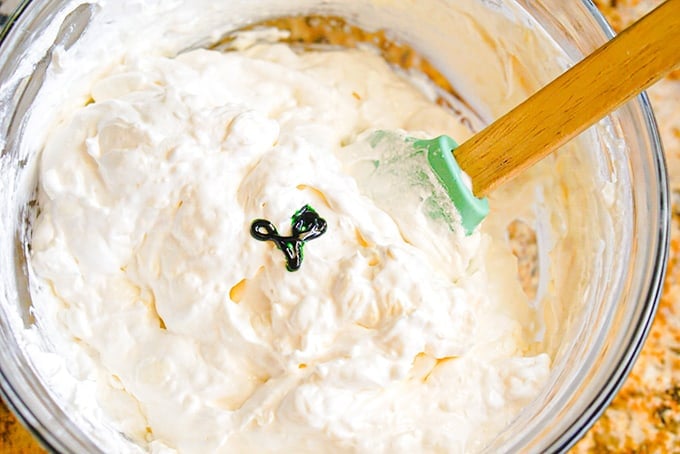 booty dip with a green food coloring on top being mixed with a green spatula for St. Patrick's Day.