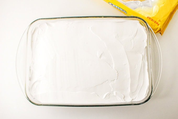 A rectangular glass dish filled with a smooth layer of white cream, exuding a hint of lemon delight. An opened package of Oreo cookies is partially visible in the top right corner.