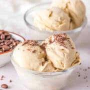 Two glass bowls of creamy coffee ice cream with chocolate shavings on top, perfectly fitting into the Category of indulgent desserts. Coffee beans are scattered around, and there is a small bowl of coffee beans in the background.