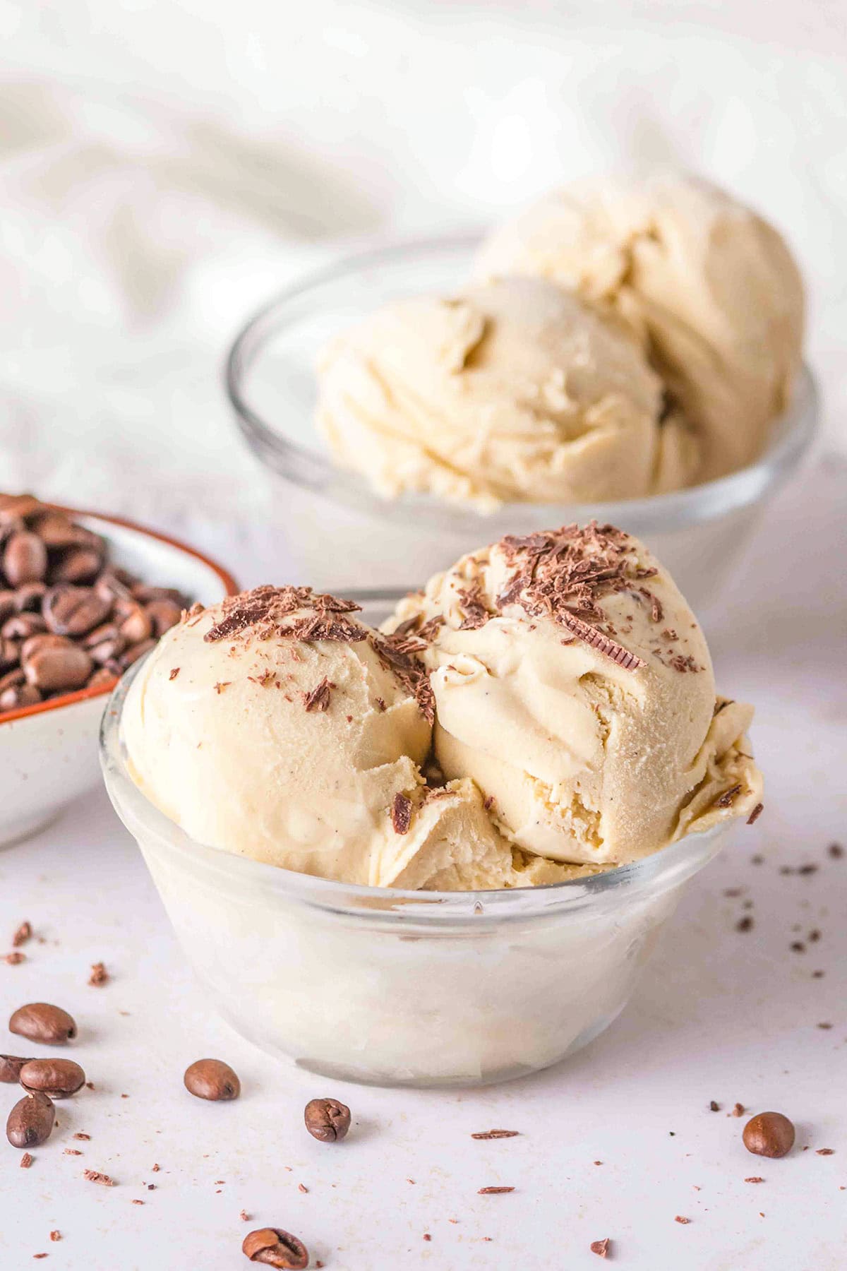 Two glass bowls of creamy coffee ice cream with chocolate shavings on top, perfectly fitting into the Category of indulgent desserts. Coffee beans are scattered around, and there is a small bowl of coffee beans in the background.