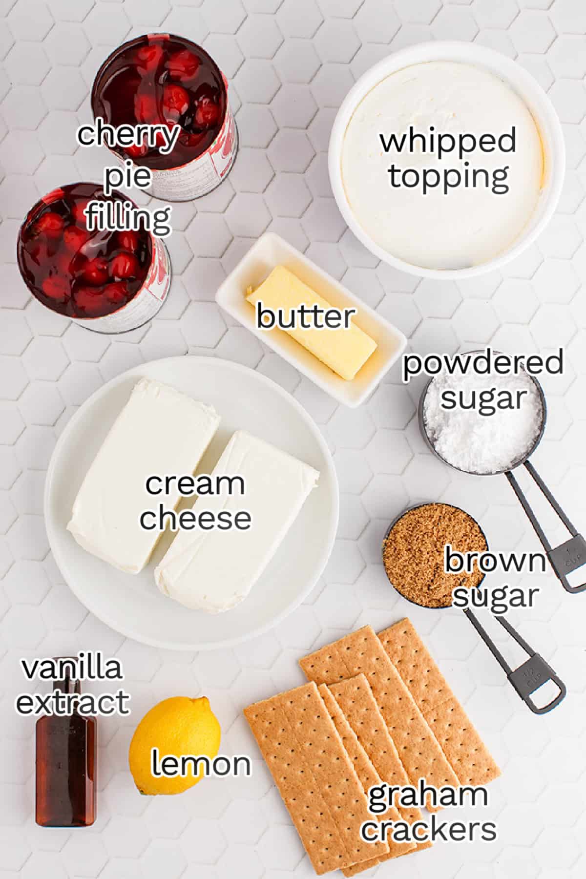 Top-down view of ingredients for a cherry delight dessert, featuring cherry pie filling, whipped topping, butter, powdered sugar, cream cheese, brown sugar, vanilla extract, lemon, and graham crackers.