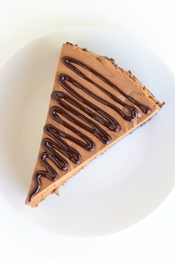 A slice of No Bake Chocolate Cheesecake topped with drizzled chocolate sauce on a white plate.