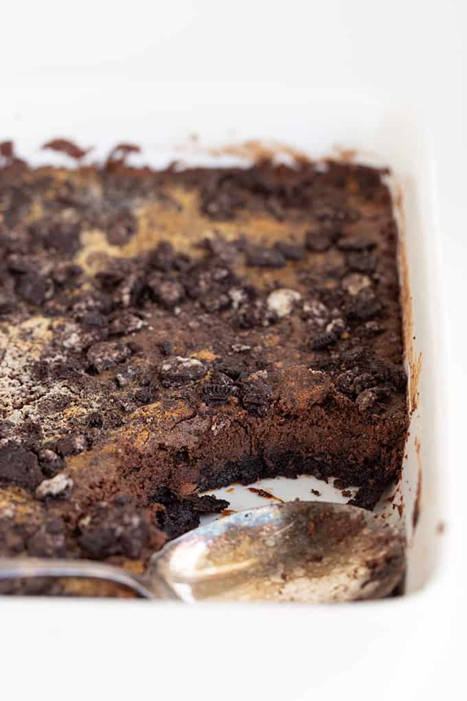 A partially eaten Oreo Dump Cake with crumb topping in a white baking dish, with a serving spoon resting on the edge.
